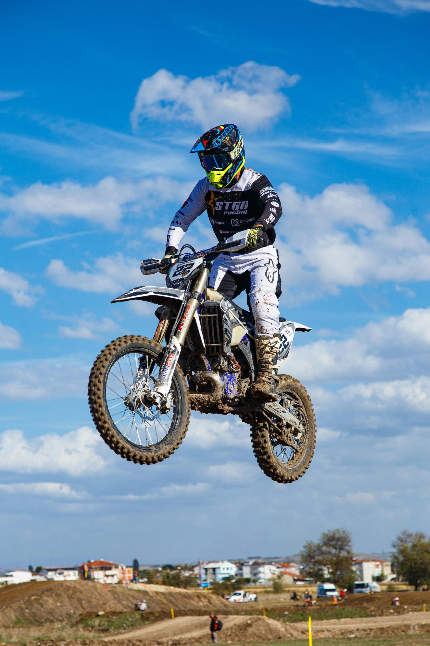 Excitant cliché d'action d'un pilote de motocross prenant son envol pendant une course sous un ciel bleu dégagé.