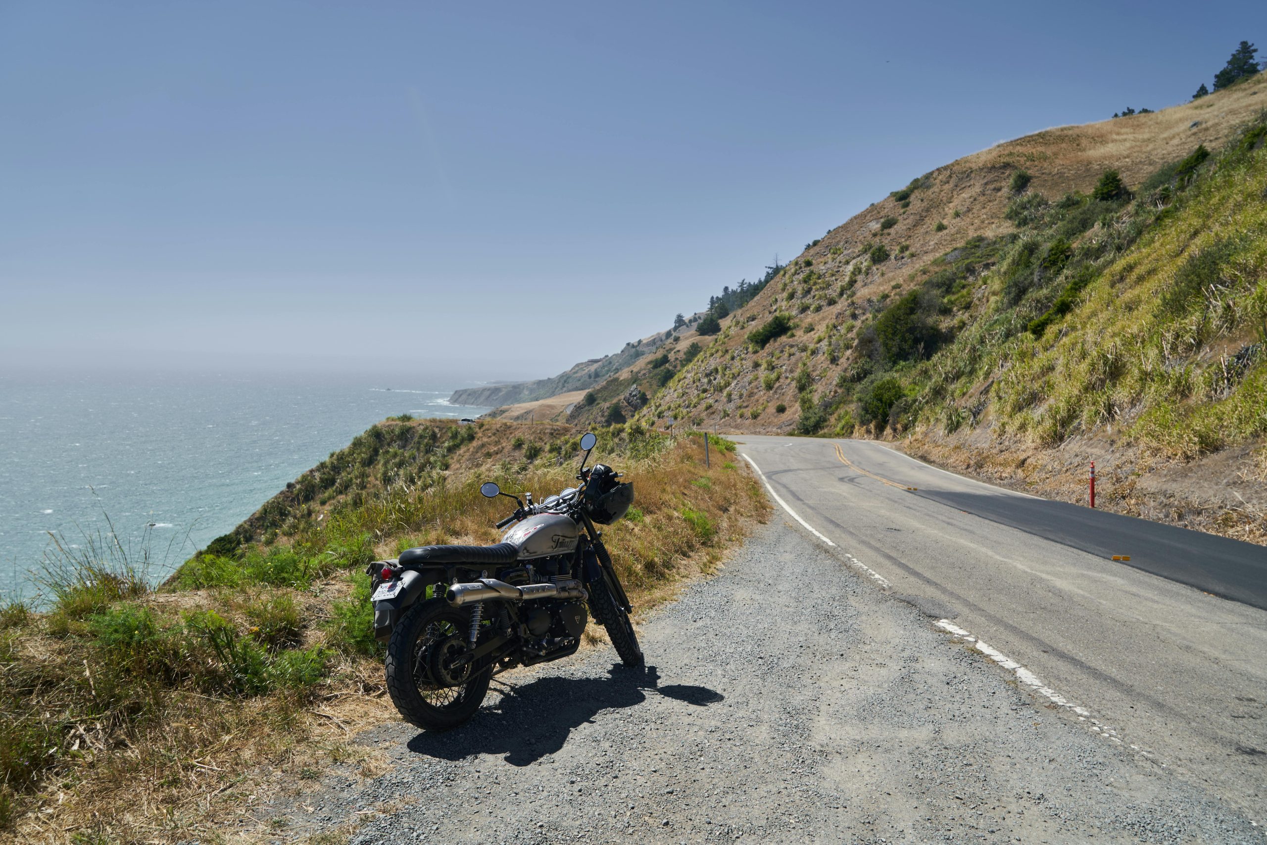 Une moto garée le long d'une route côtière avec vue sur l'océan par une journée ensoleillée.