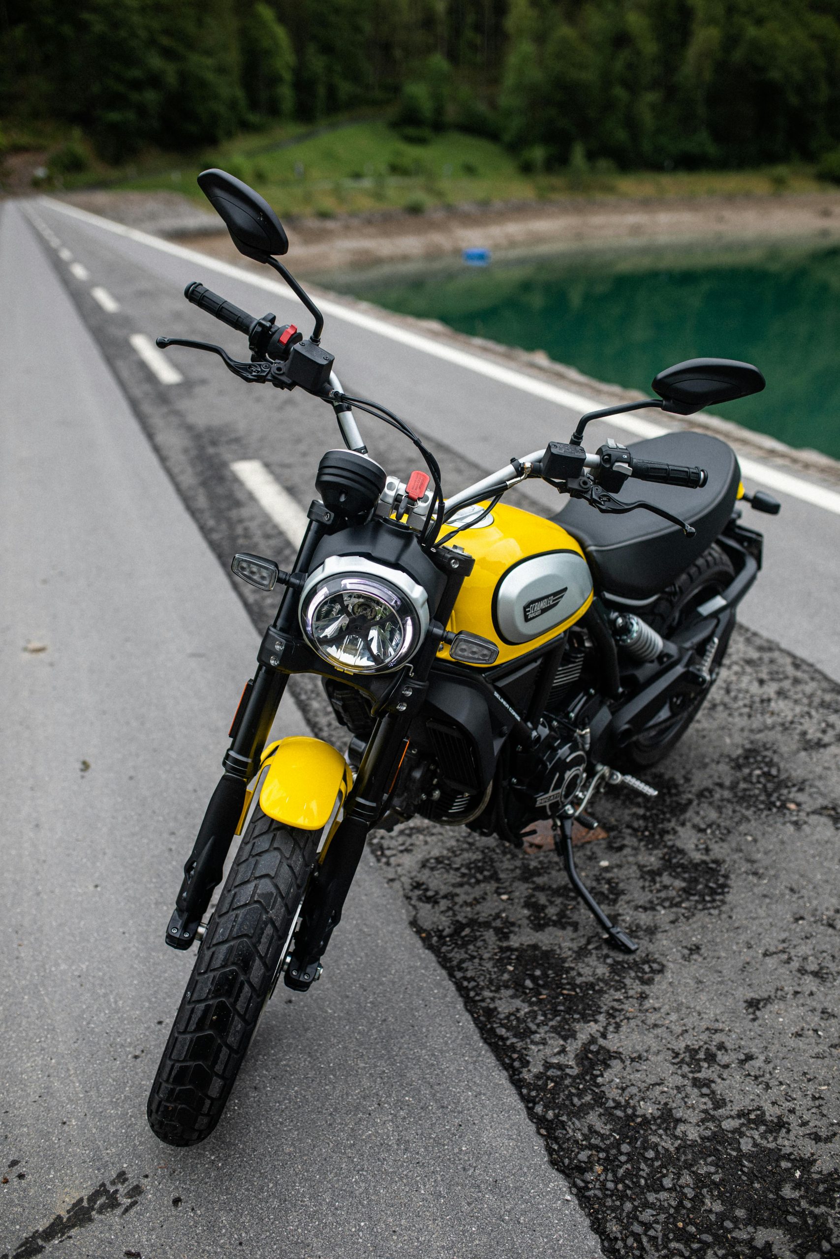 Une moto scrambler jaune vif garée sur le bord d'une route pittoresque entourée de verdure luxuriante.