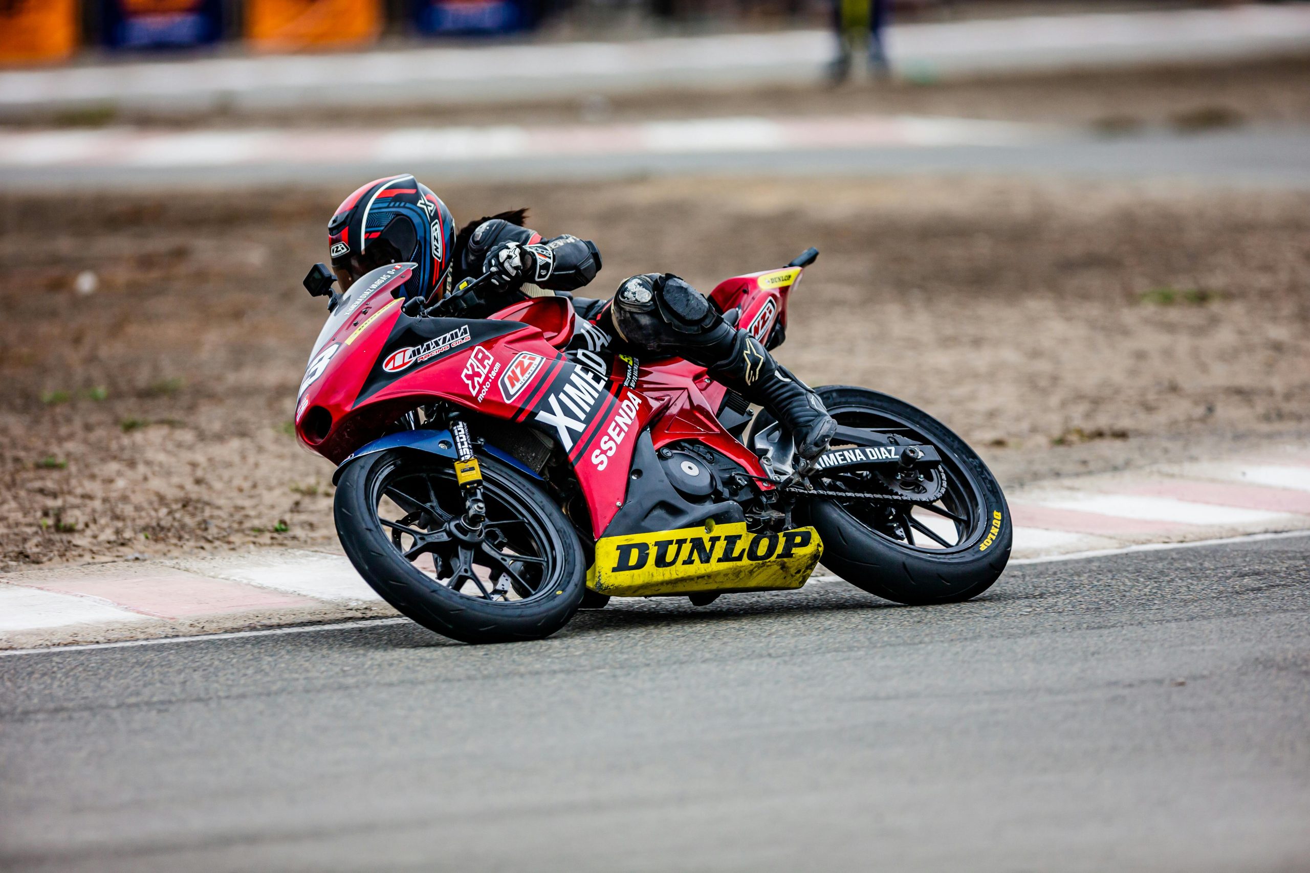 Motocycliste en course penché dans un virage sur un circuit professionnel de compétition.