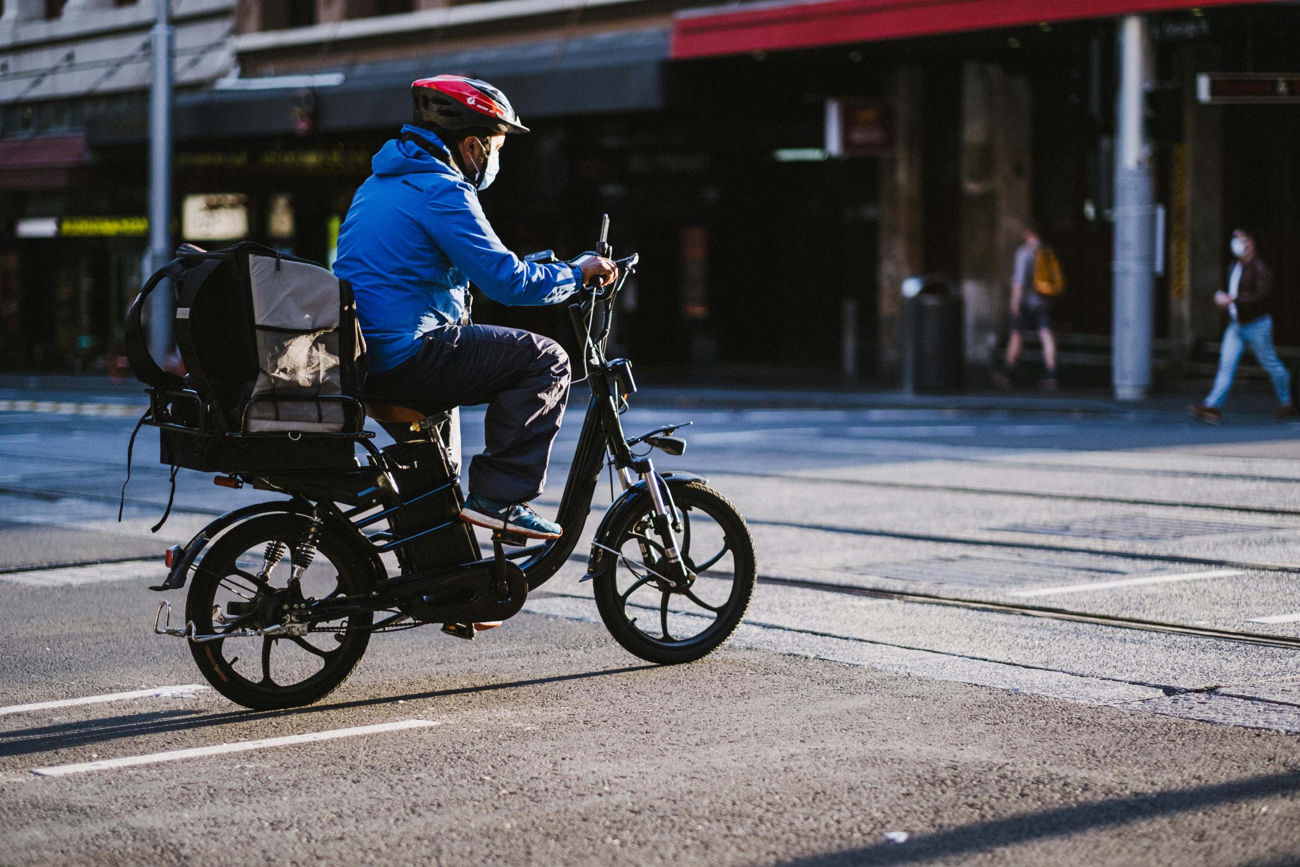 A delivery cyclist wearing a face mask rides through Sydney streets highlighting urban transportation during the pandemic. Un cycliste livreur portant un masque facial circule dans les rues de Sydney, mettant en avant les transports urbains pendant la pandémie.