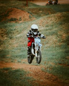 Child motocross rider in full gear riding through a grassy dirt track. Enfant pilote de motocross en équipement complet roulant sur une piste de terre herbeuse.