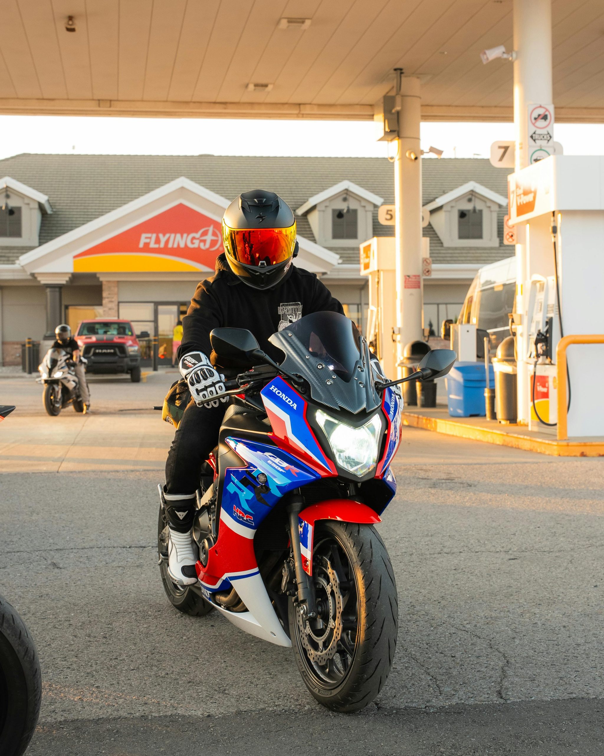 Motorcyclist refuels at a gas station during sunset. Vibrant bike colors and setting create dynamic scene. Motocycliste fait le plein à une station-service au coucher du soleil. Les couleurs vibrantes du vélo et le décor créent une scène dynamique.