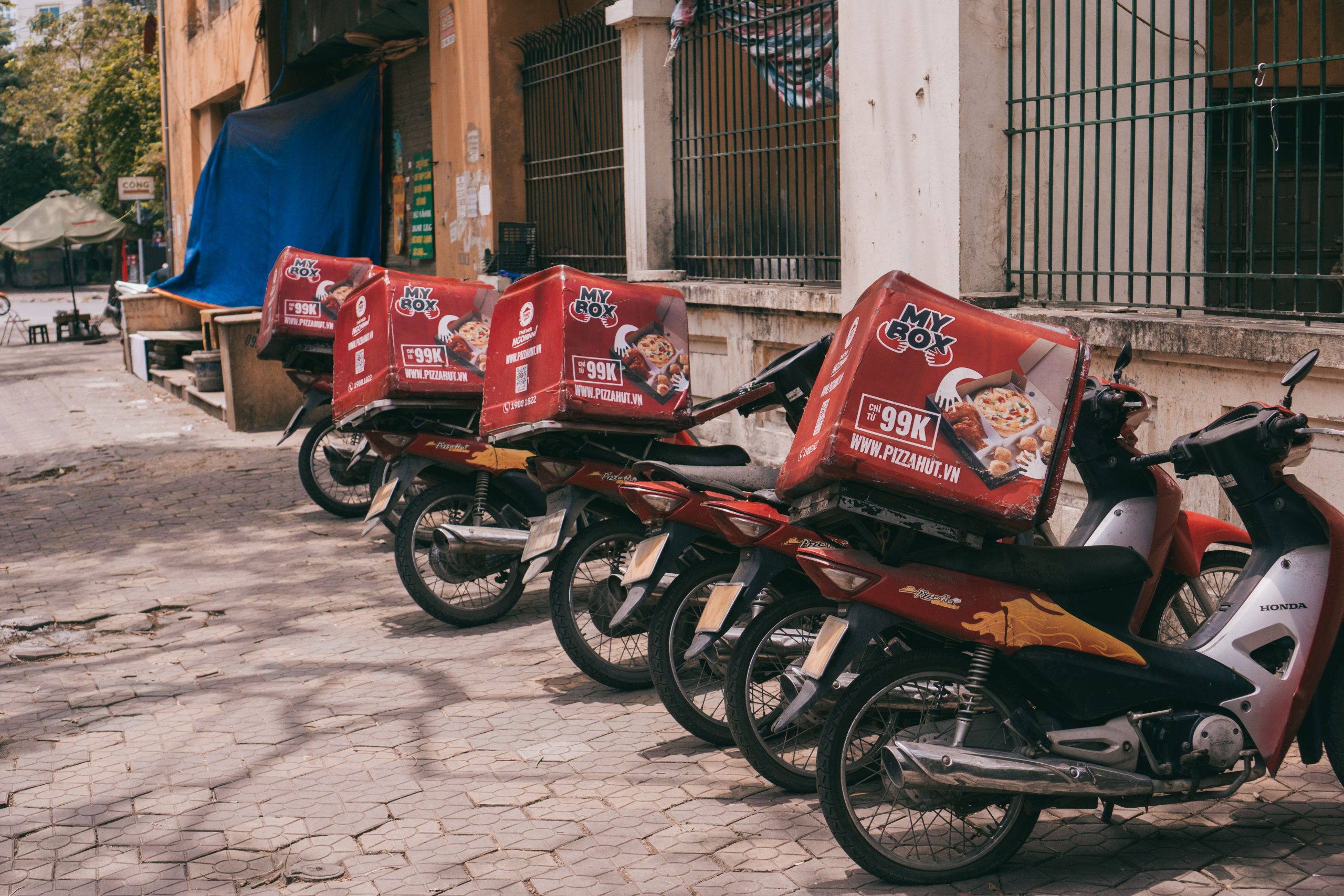 Motorbikes with branded delivery boxes parked on an urban sidewalk, showcasing food delivery services. Motos avec des boîtes de livraison de marque garées sur un trottoir urbain, mettant en avant les services de livraison de nourriture.