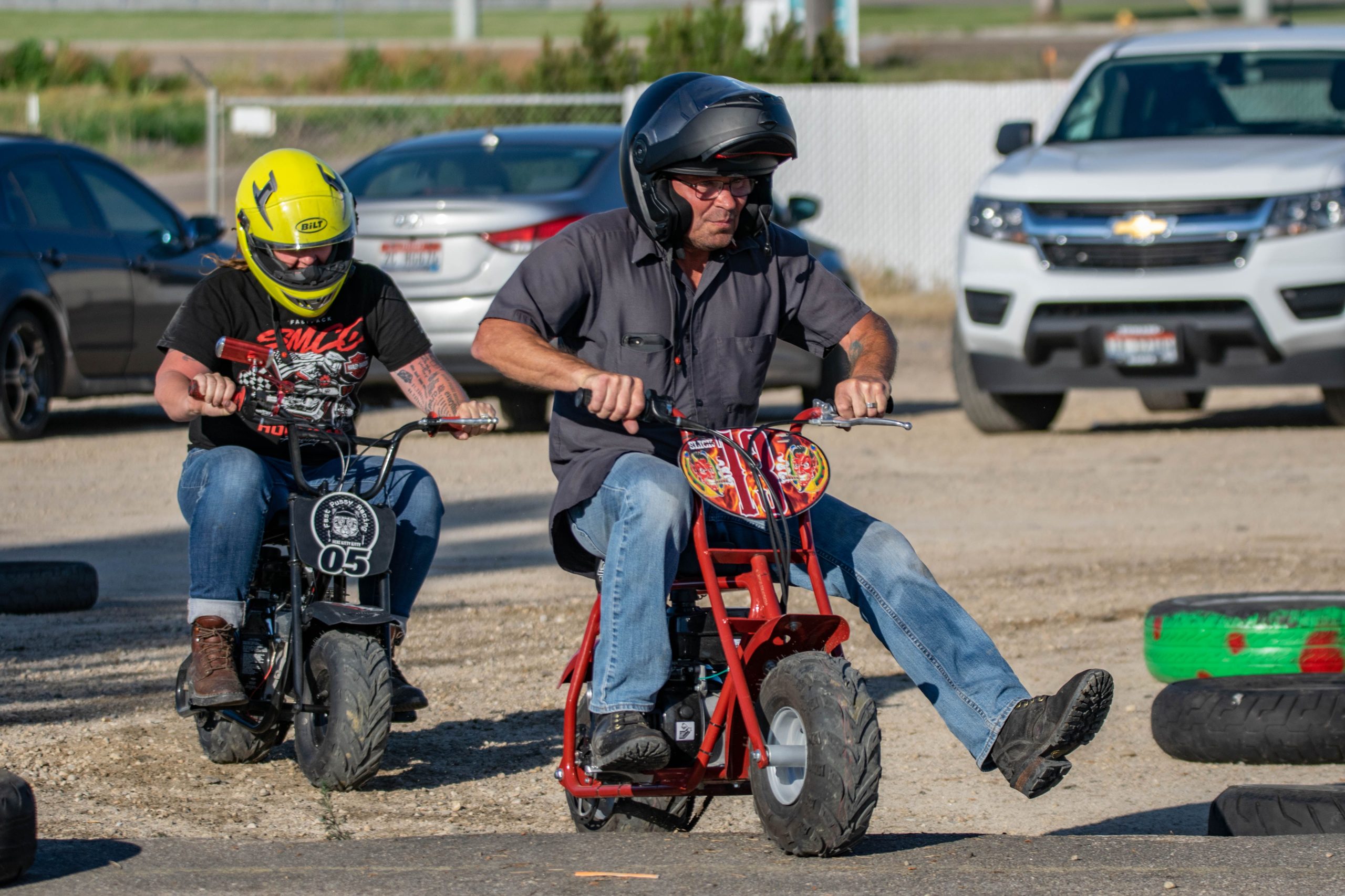Two adults racing mini bikes outdoors, showcasing excitement and skill. Deux adultes font la course sur des mini-motos en plein air, montrant de l'excitation et du savoir-faire.