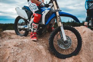 Motocycliste masculin méconnaissable en tenue de sport assis sur un motocross sur un tas de sable contre un ciel nuageux avec une forêt au loin en plein jour.