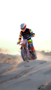 Dynamic shot of a motocross rider with vibrant gear racing over sand dunes. Plan dynamique d'un pilote de motocross avec un équipement vibrant racing sur des dunes de sable.