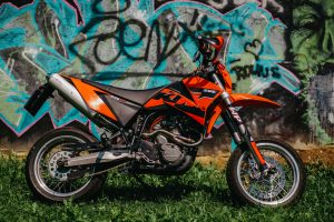 Orange KTM motorcycle parked against graffiti-covered wall, showcasing urban motorsport style. Moto KTM orange garée contre un mur couvert de graffitis, mettant en avant un style de motosport urbain.