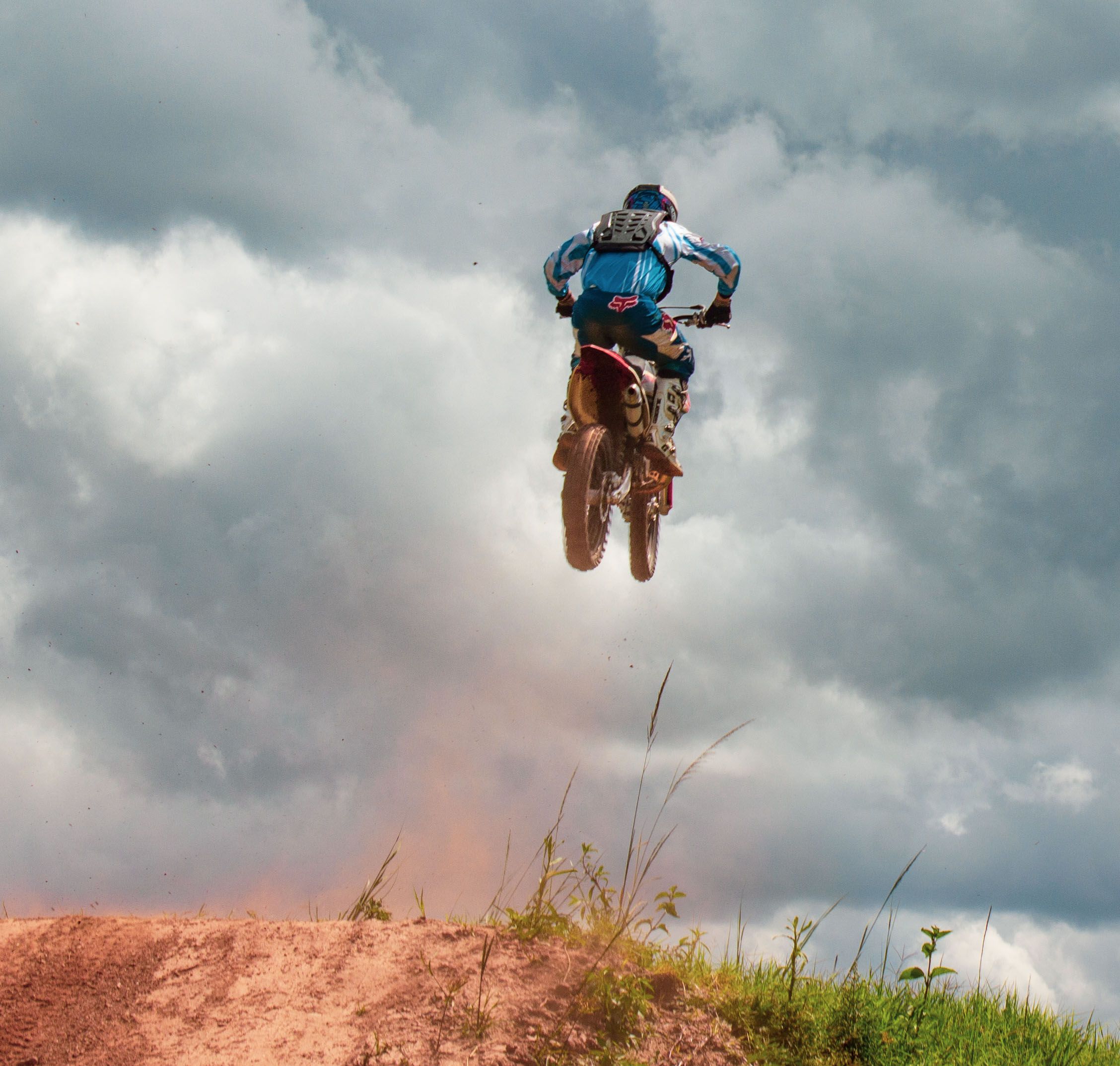 Motocycliste audacieux de motocross s'envolant dans les airs sur un sentier de terre sous des nuages dramatiques.