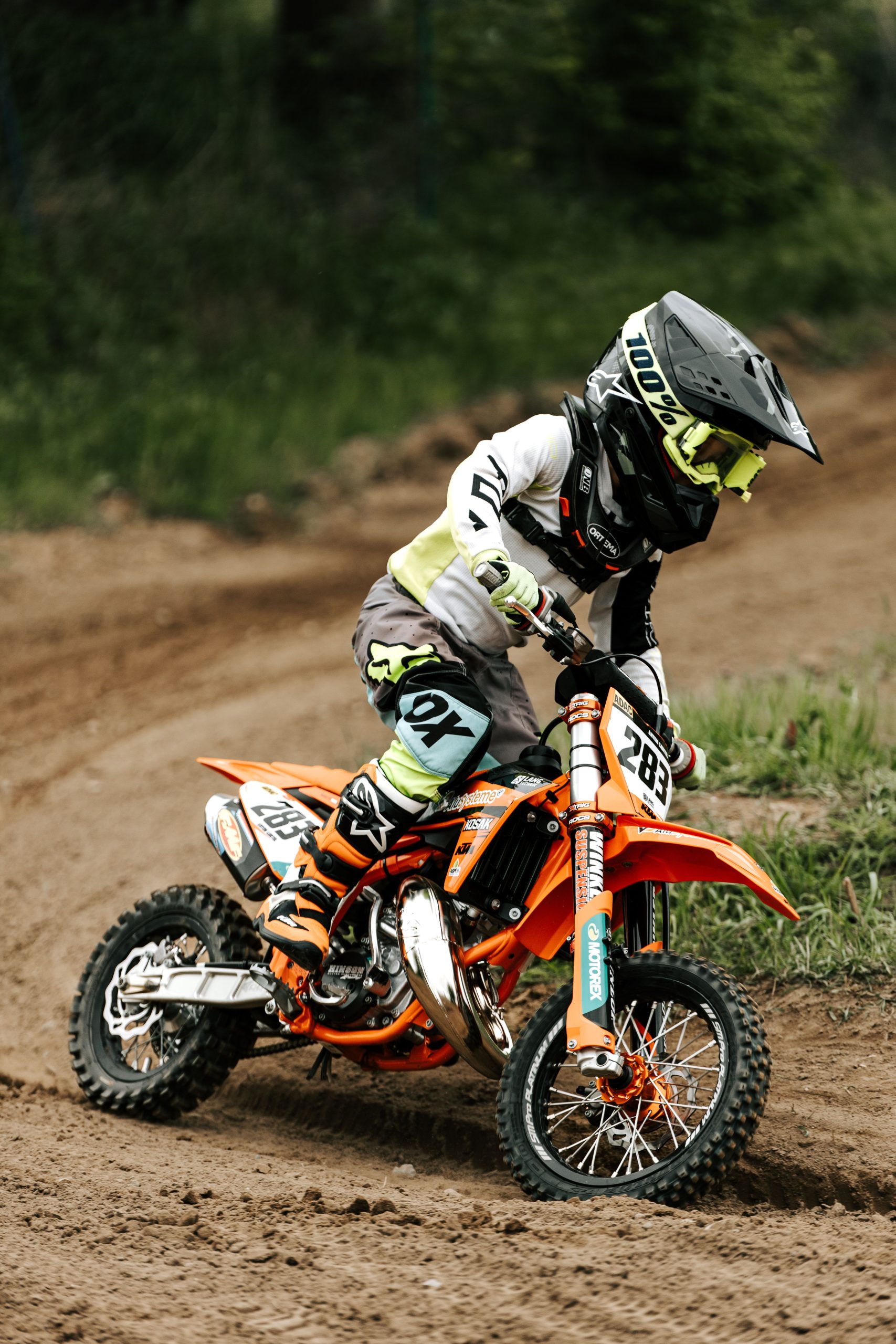 A young child riding a dirt bike on a muddy track, showcasing skills and focus in outdoor motocross sports. Un jeune enfant chevauchant un vélo de terre sur une piste boueuse, mettant en valeur ses compétences et sa concentration dans les sports de motocross en plein air.