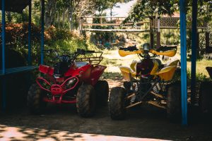 Two quad bikes parked under a shaded area surrounded by lush greenery. Deux quads garés sous une zone ombragée entourée de verdure luxuriante.