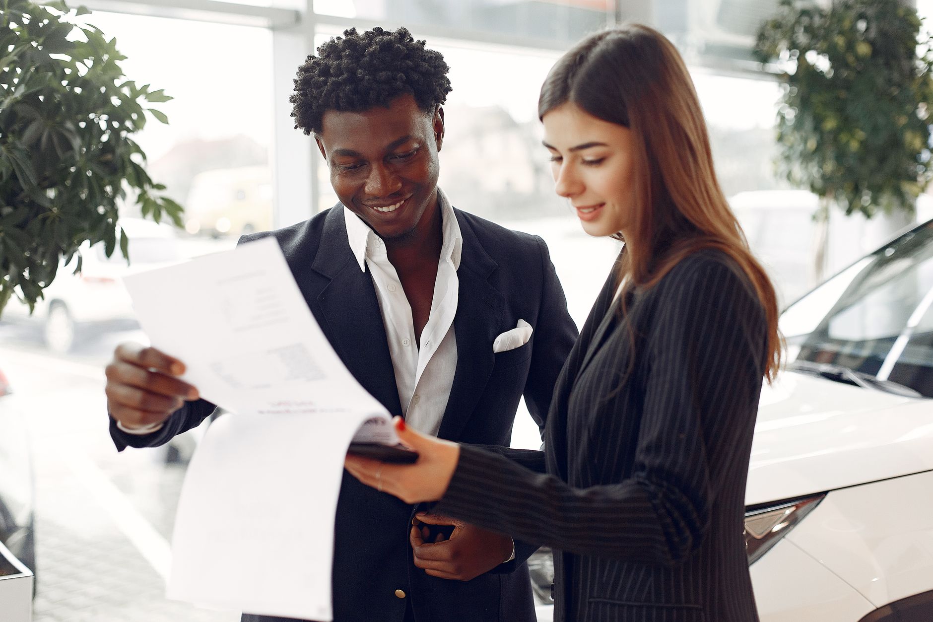 Client et vendeur qui examinent un contrat dans un showroom automobile