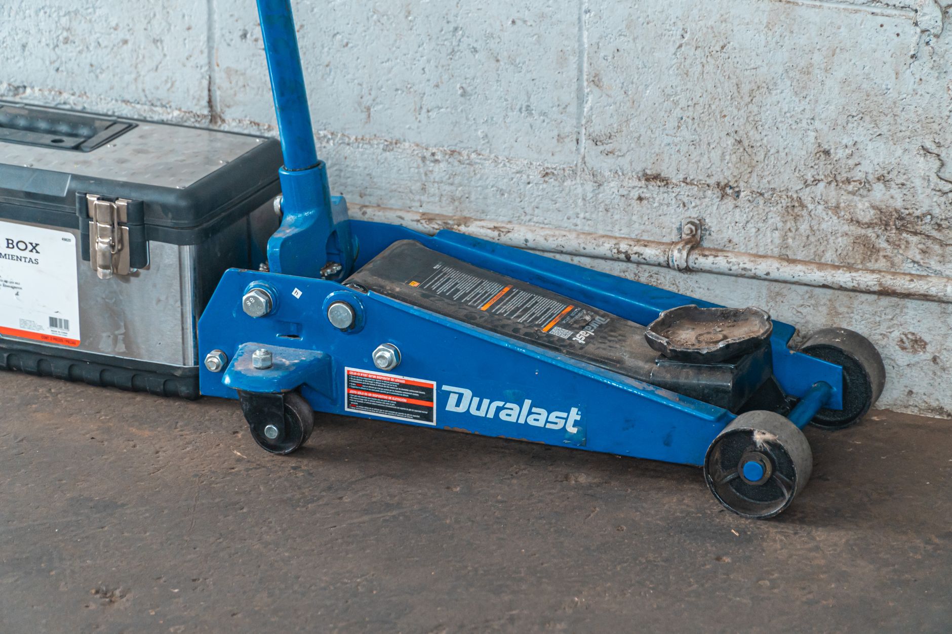 Cric hydraulique bleu posé au sol avec une caisse à outils
