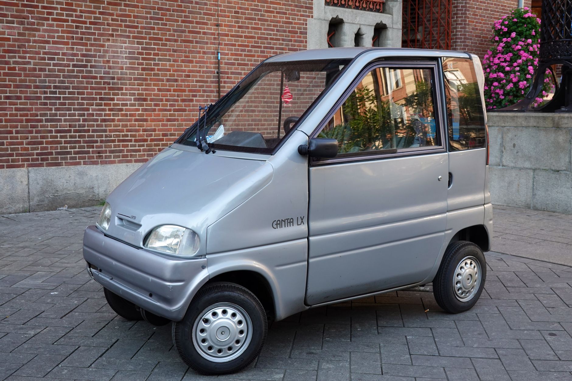 Microcar argentee garee dans une rue pavee